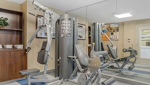 Un gimnasio con diferentes máquinas de ejercicio, un espejo y un tablón de anuncios en la pared.