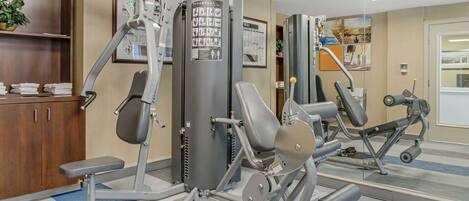 A gym with various exercise machines, a mirror, and a bulletin board on the wall.