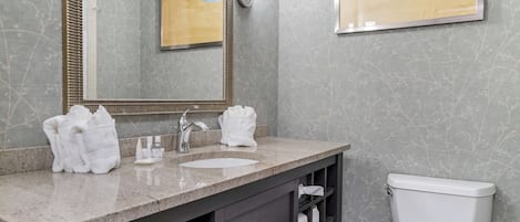 Un baño con un lavabo de mármol, dos toallas blancas, un espejo y un inodoro.
