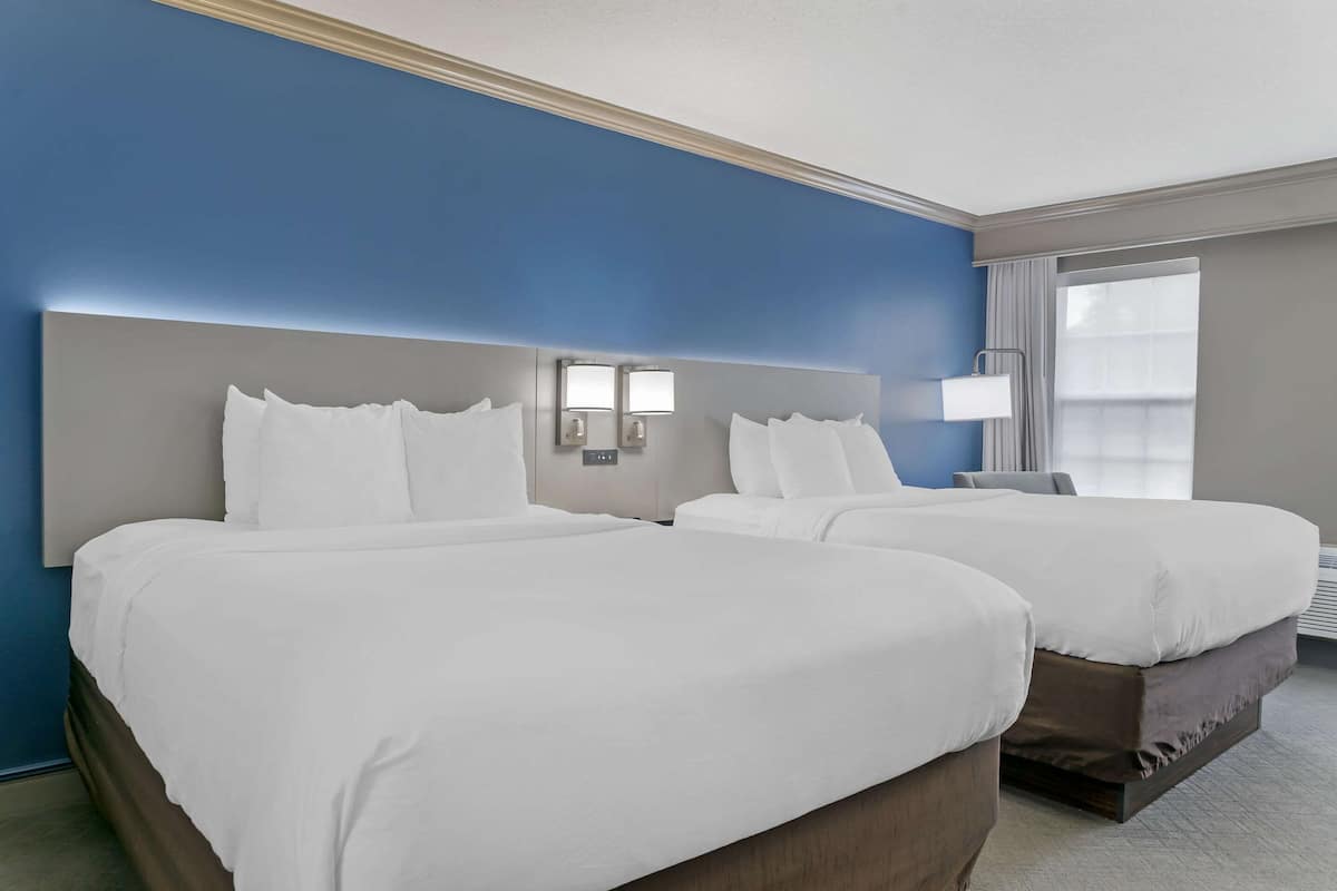 A hotel room with two beds, a large headboard, bedside lamps, and a window with curtains.