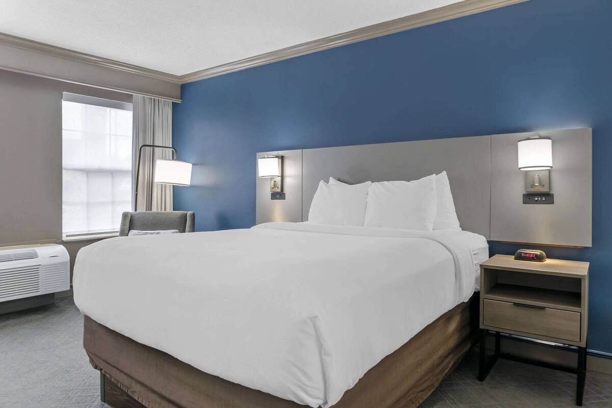 A hotel room with a large bed, bedside lamps, a nightstand, and a window with curtains.