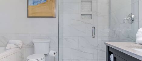 Un baño moderno con cabina de ducha de vidrio, inodoro y lavabo con encimera de mármol.