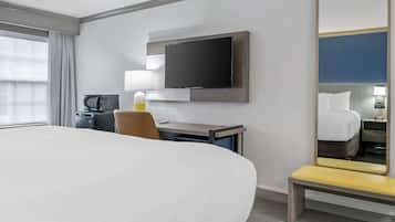 A hotel room with a large bed, a desk with a lamp, a television, a mirror, and a bench.