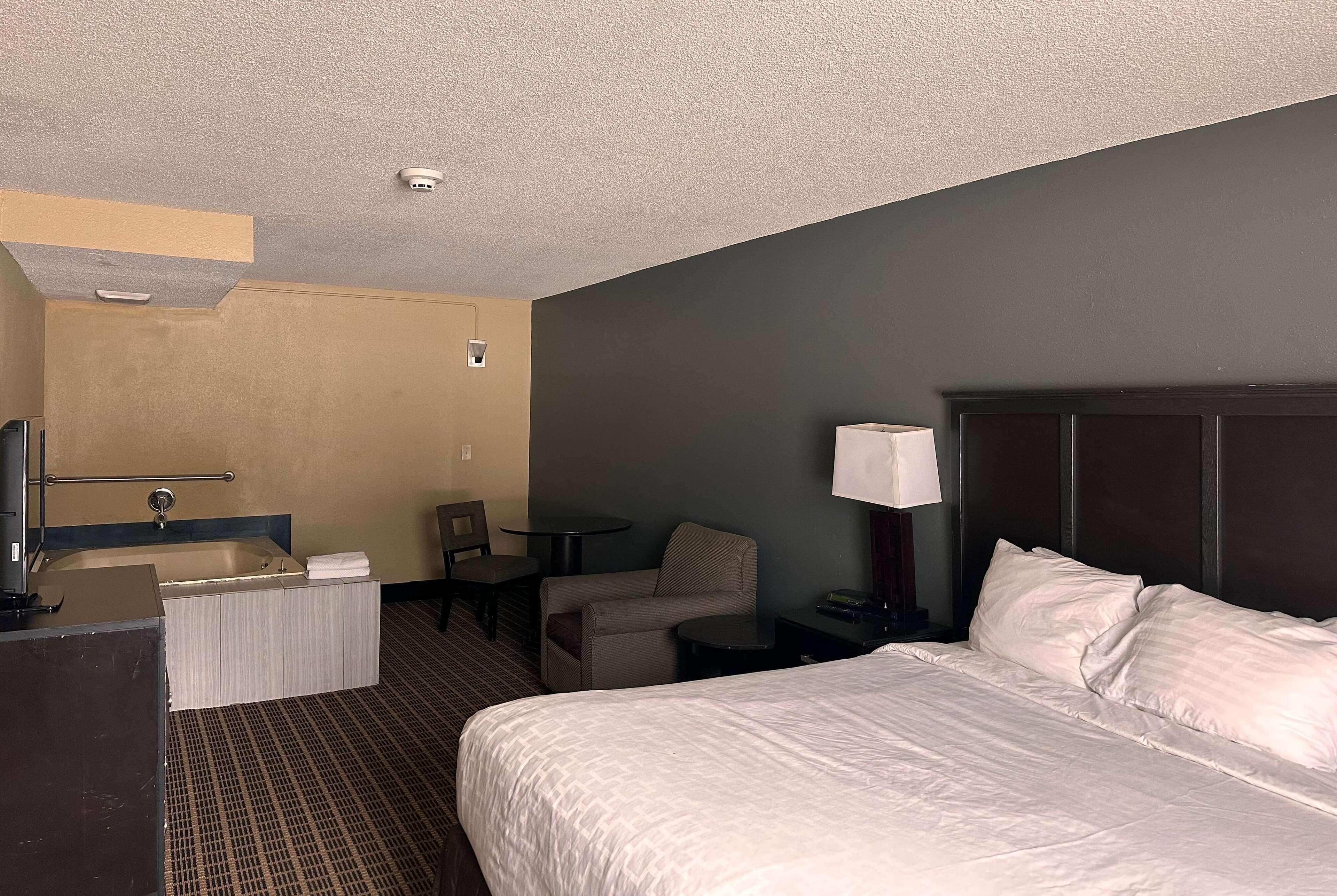 Ein Hotelzimmer mit einem großen Bett, einem Schreibtisch mit Stuhl, einem kleinen Tisch, einer Couch, einem Badezimmer mit Badewanne und einem Nachttisch mit Lampe.