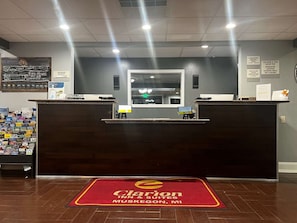 A hotel reception desk with a digital screen, a chalkboard with hotel information, and a welcome mat. - Days Inn Muskegon (Muskegon Heights)