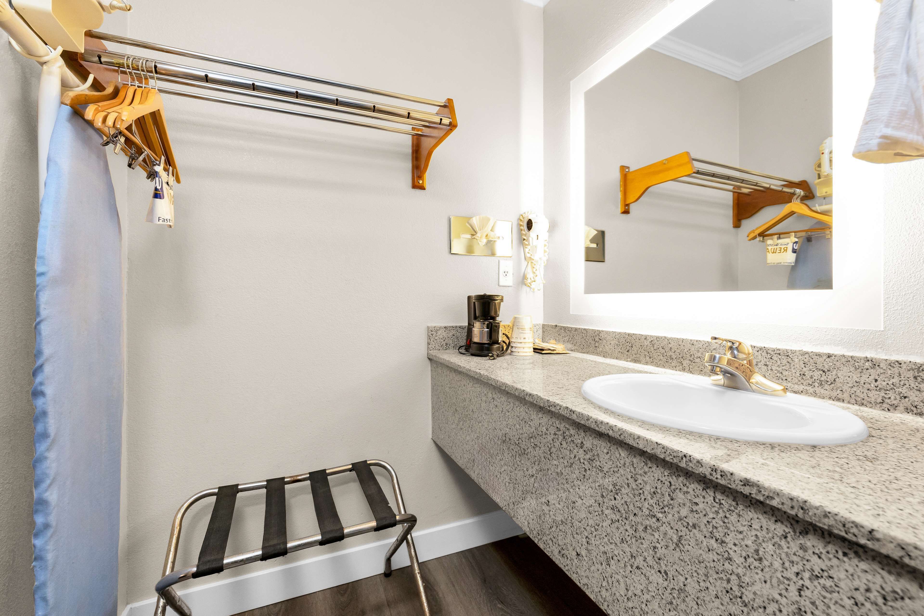 A bathroom with a granite countertop, a white sink, a gold faucet, a towel rack, a hairdryer, and a small step stool.