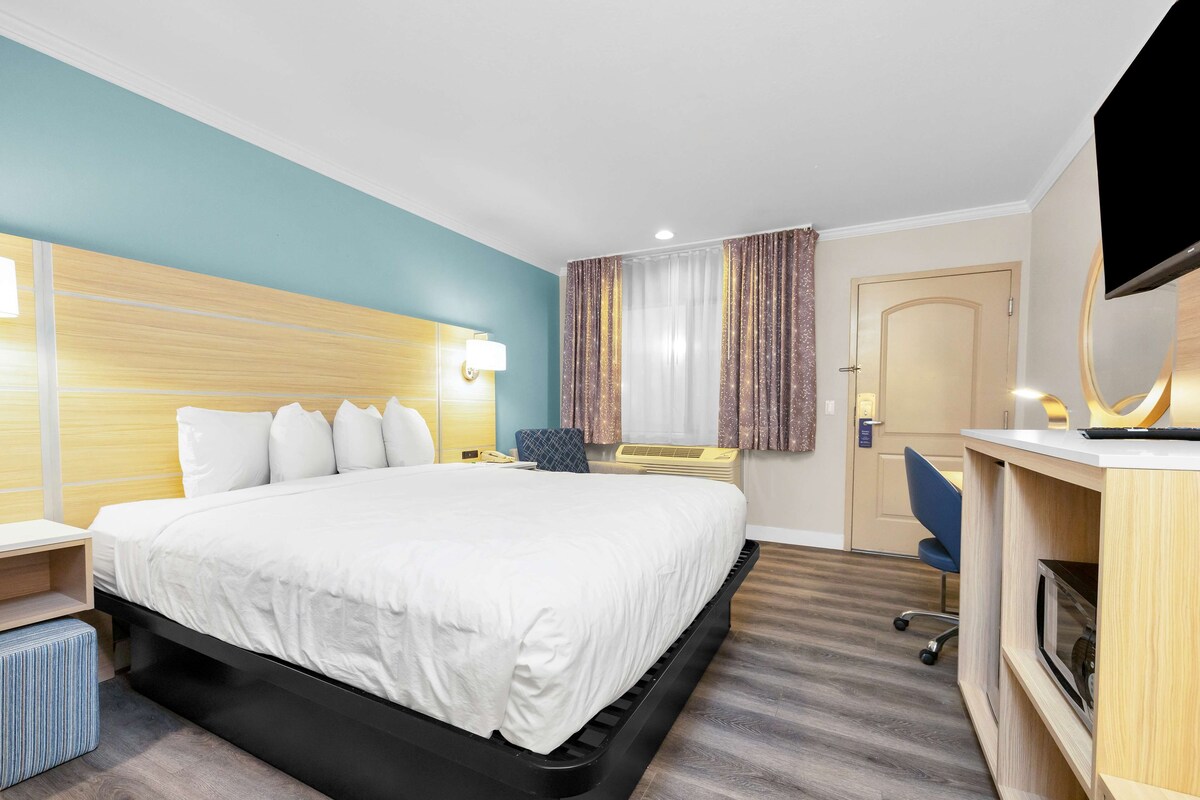 Habitación de hotel con una cama grande, un escritorio con televisor de pantalla plana, una silla y un ventanal con cortinas.