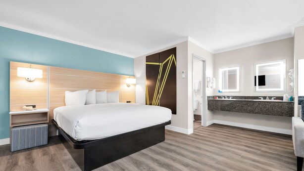 Una habitación de hotel moderna con una cama grande, mesitas de noche, un banco integrado, un tocador con espejo y una zona de ducha.