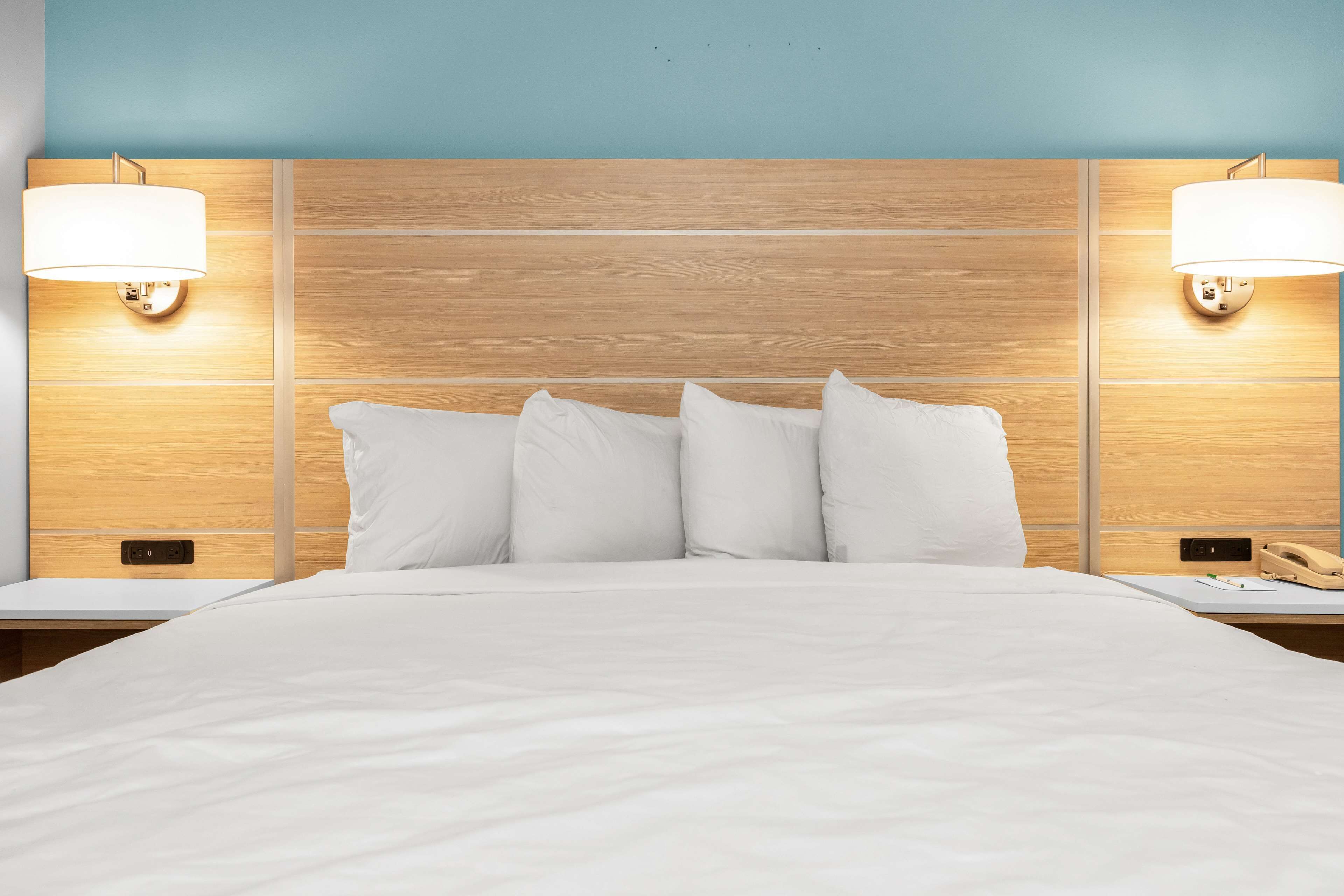 A hotel room with a large bed, two bedside lamps, a bedside phone, and a wooden headboard.