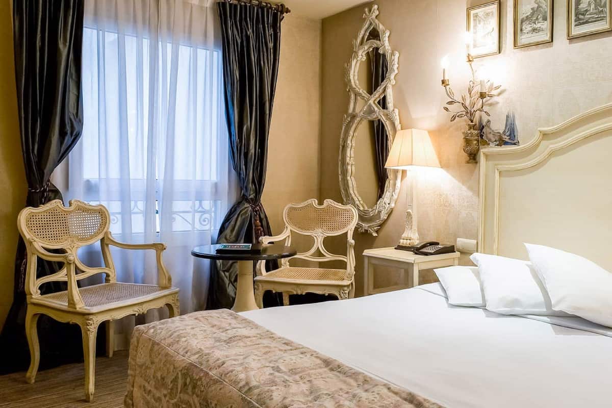 Une chambre d’hôtel avec un grand lit, deux chaises, une table de chevet avec une lampe et un miroir au mur.