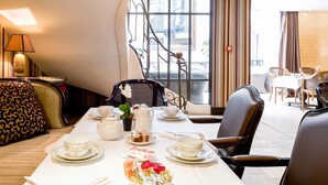 Een zithoek met een tafel gedekt voor thee, inclusief theepotten, kopjes en schotels. Er staan stoelen rond de tafel en er is uitzicht op het exterieur door grote ramen.