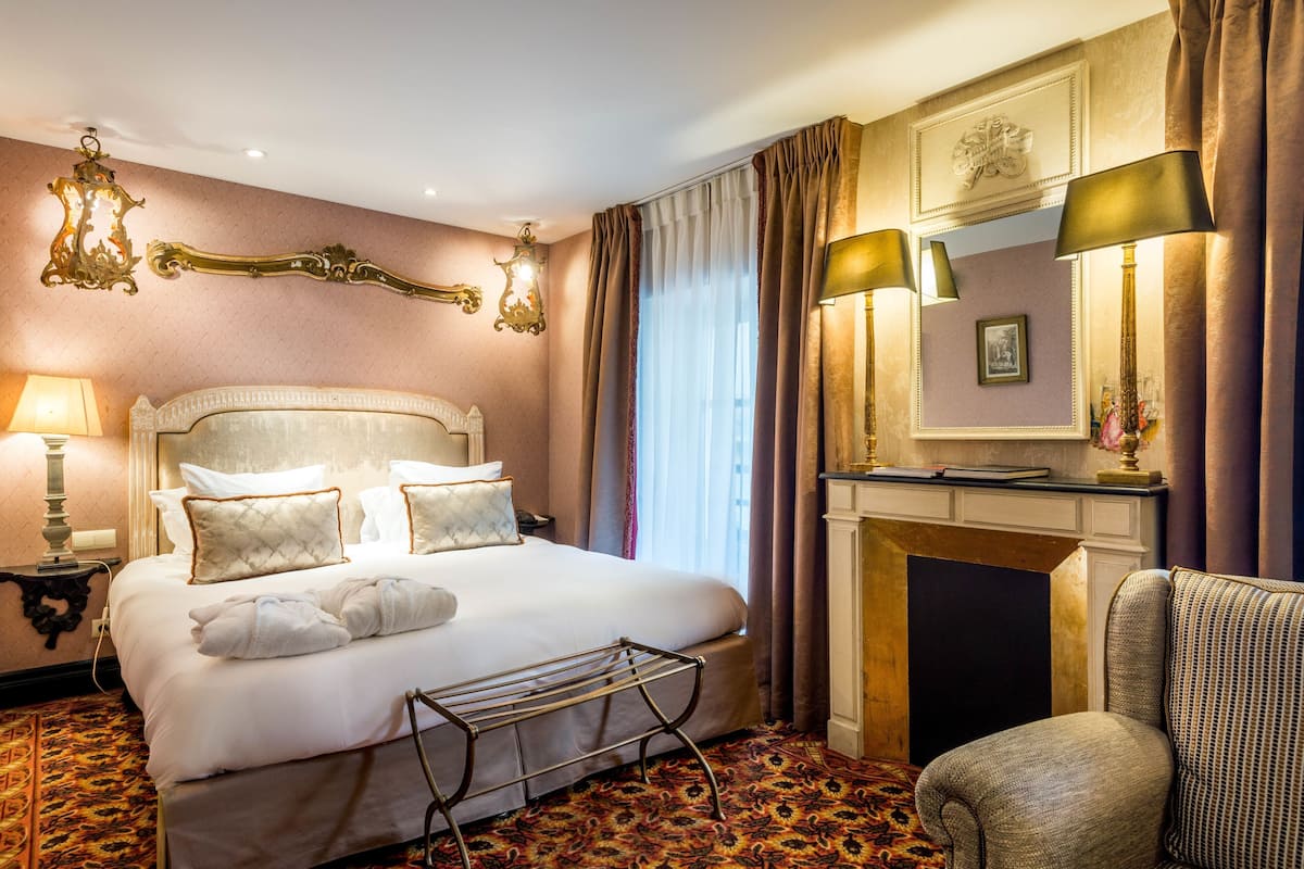 Une chambre d’hôtel avec un grand lit, une chaise, une cheminée et un lustre.
