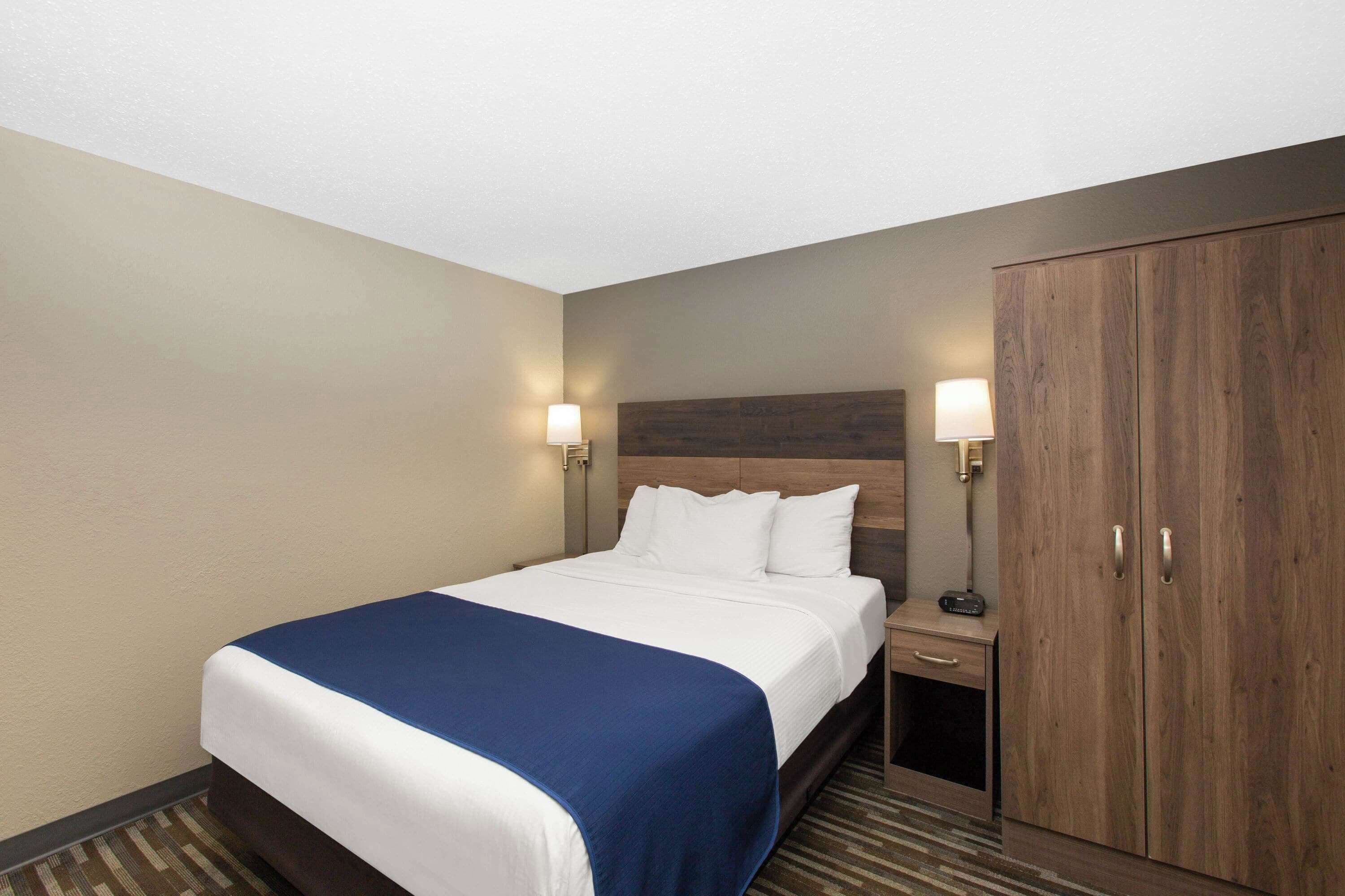 A hotel room with a large bed, two bedside lamps, a wardrobe, and a small table with a radio.