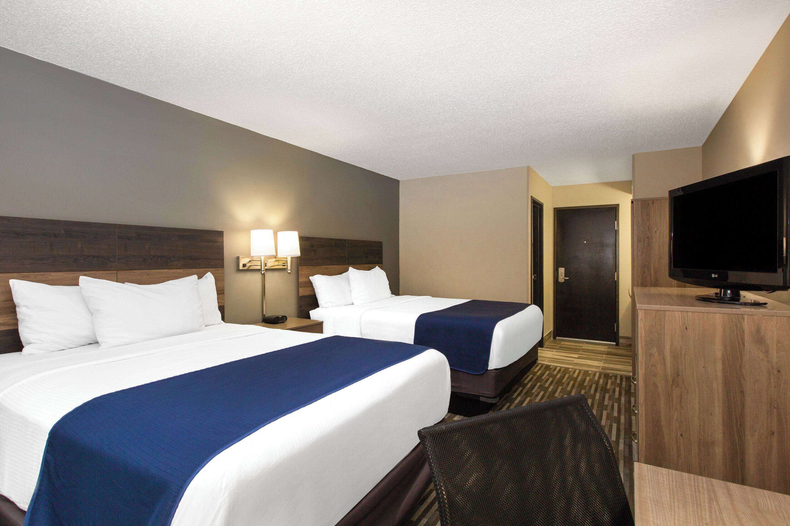 A hotel room with two beds, a television, and a desk.