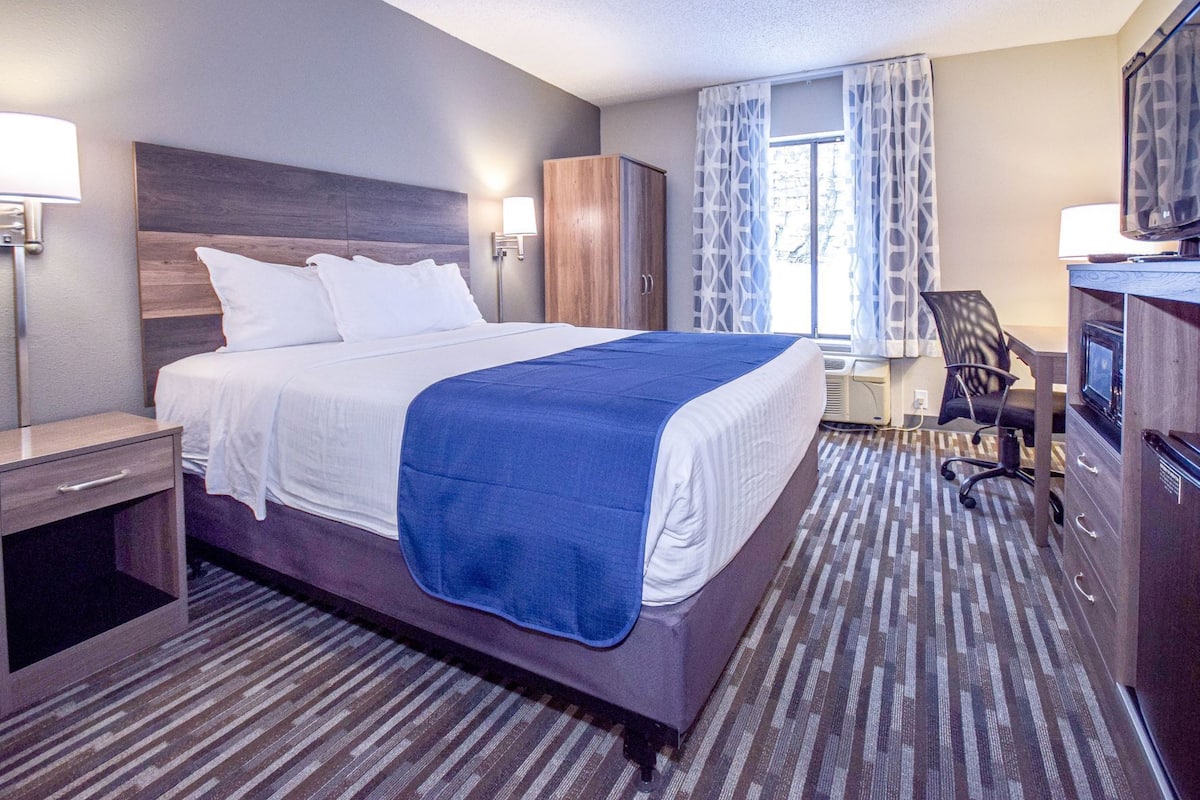 A hotel room with a bed, a desk, a chair, a TV, and a wardrobe.