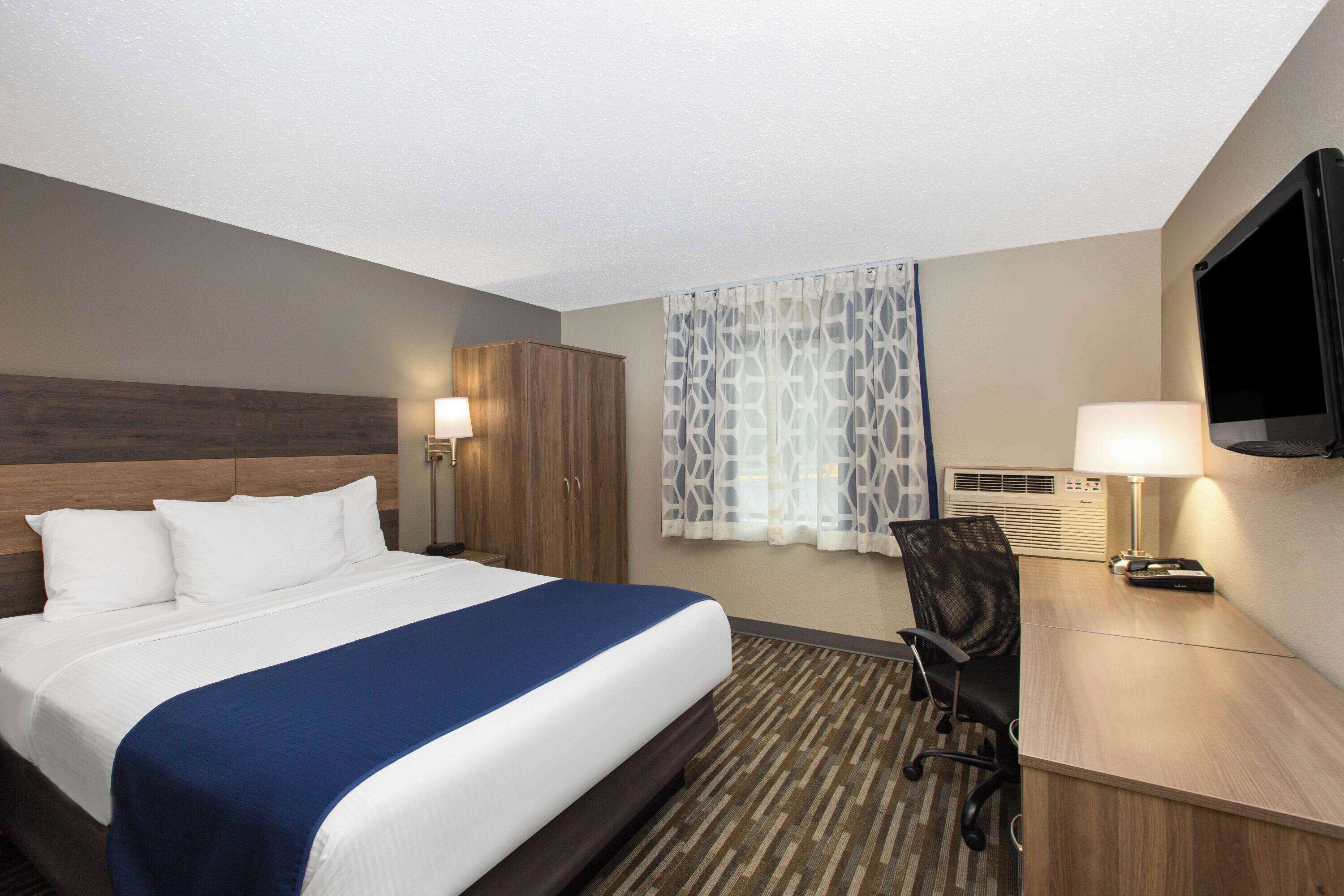 A hotel room with a bed, a desk, a chair, a TV, and a window with curtains.