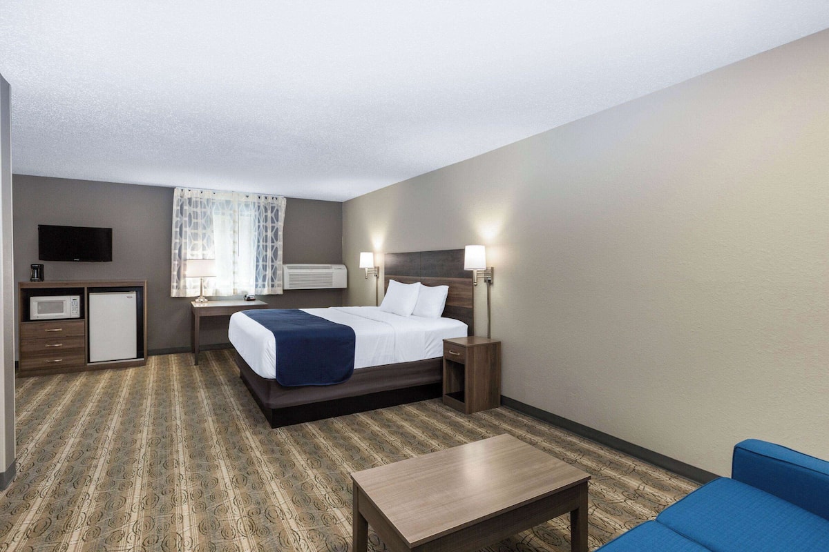 A hotel room with a bed, bedside table, lamp, and a small desk with a television and microwave.