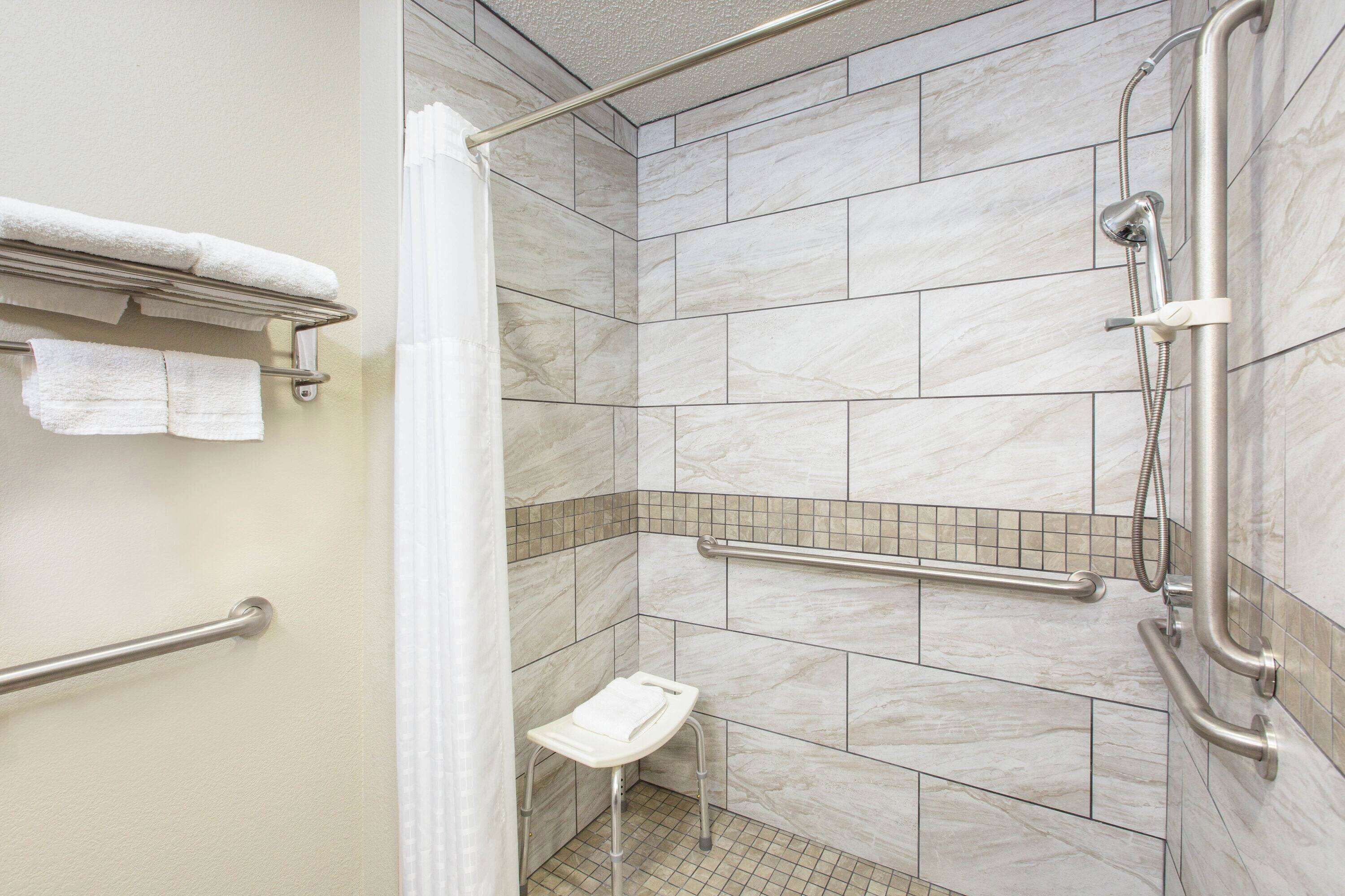 Une salle de bain moderne équipée d’une douche, de barres d’appui, d’un banc et d’un porte-serviettes.