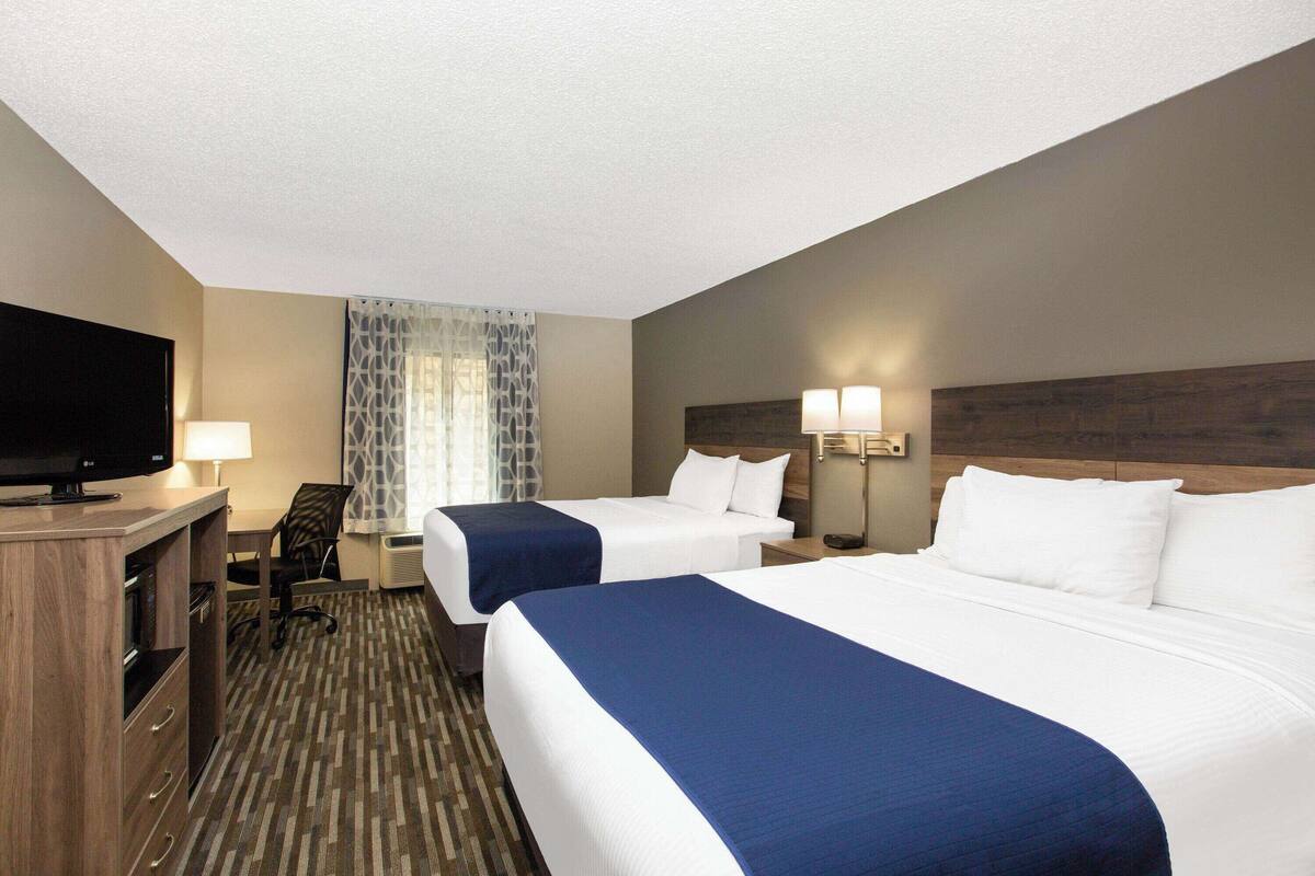 A hotel room with two beds, a TV, a desk, and a chair.