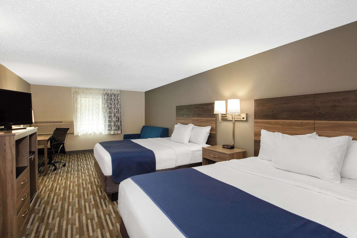 A hotel room with two beds, a desk with a chair, a TV, and a window with curtains.