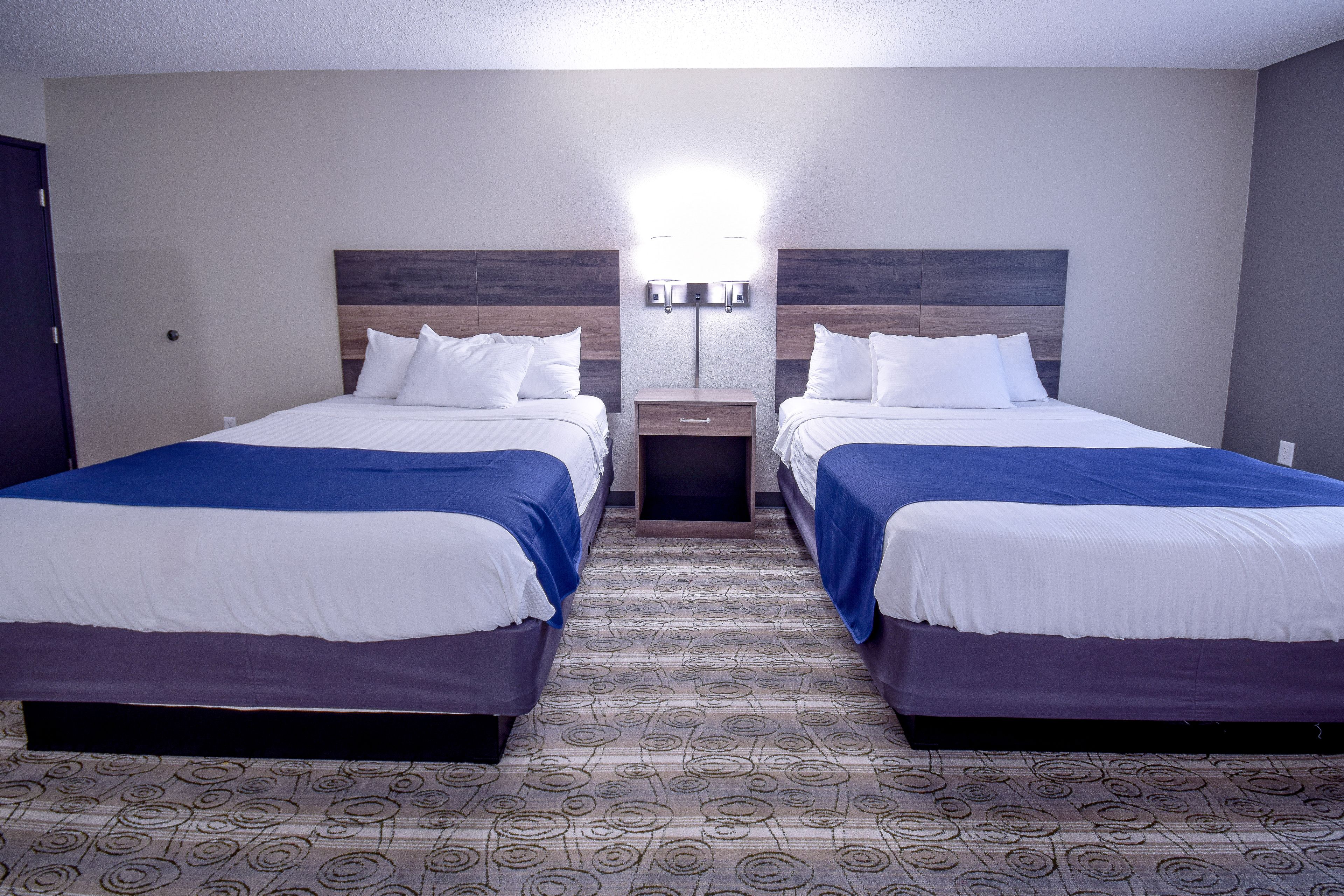 Habitación de hotel con dos camas, una mesita de noche y una lámpara fijada a la pared.
