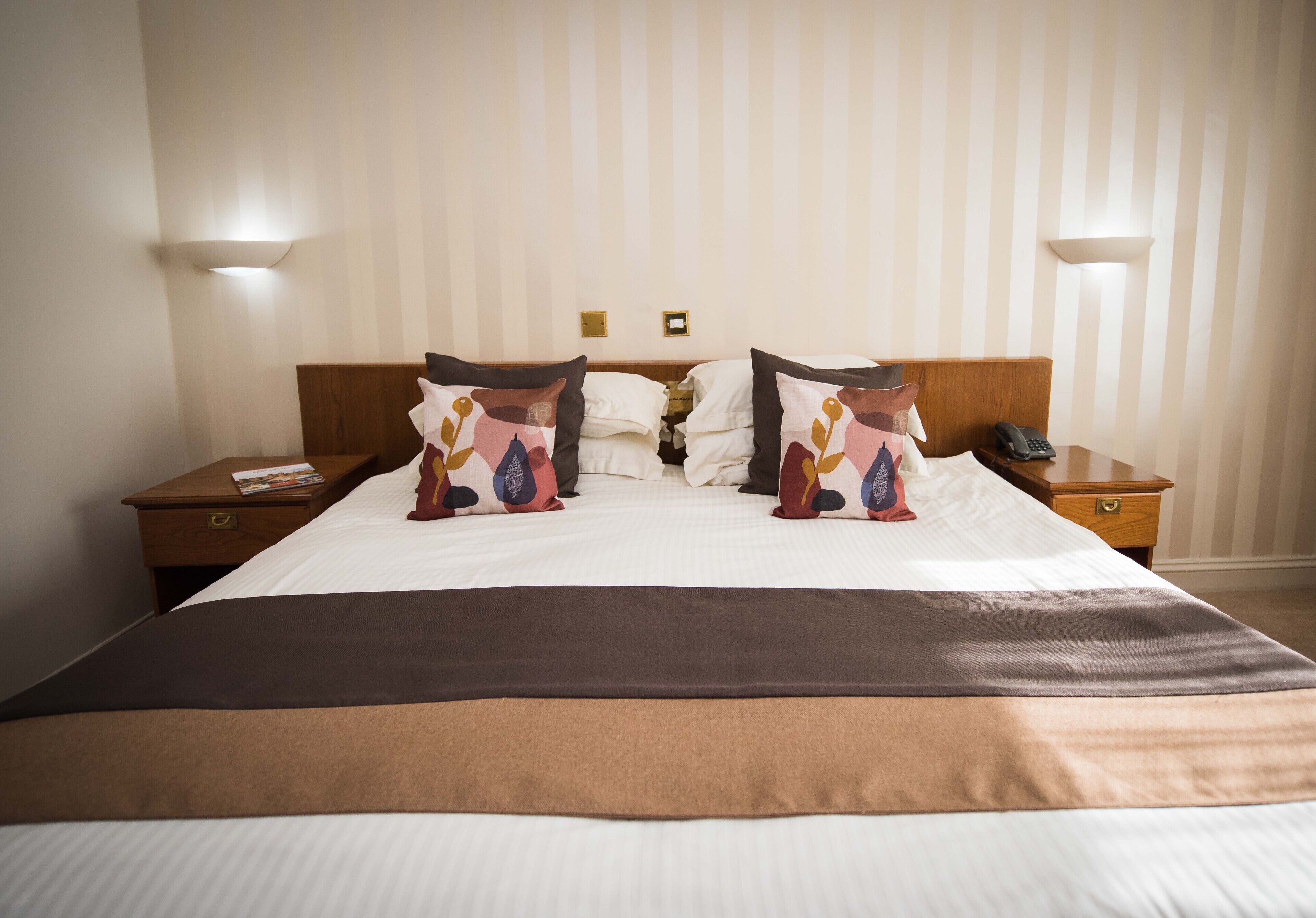 A hotel room with a large bed, two bedside tables, a nightstand, and a wall-mounted telephone.