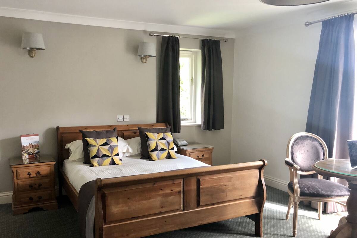 A neatly arranged bedroom with a wooden bed, bedside tables, a chair, and a window with curtains.
