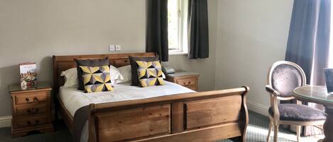 A neatly arranged bedroom with a wooden bed, bedside tables, a chair, and a window with curtains.