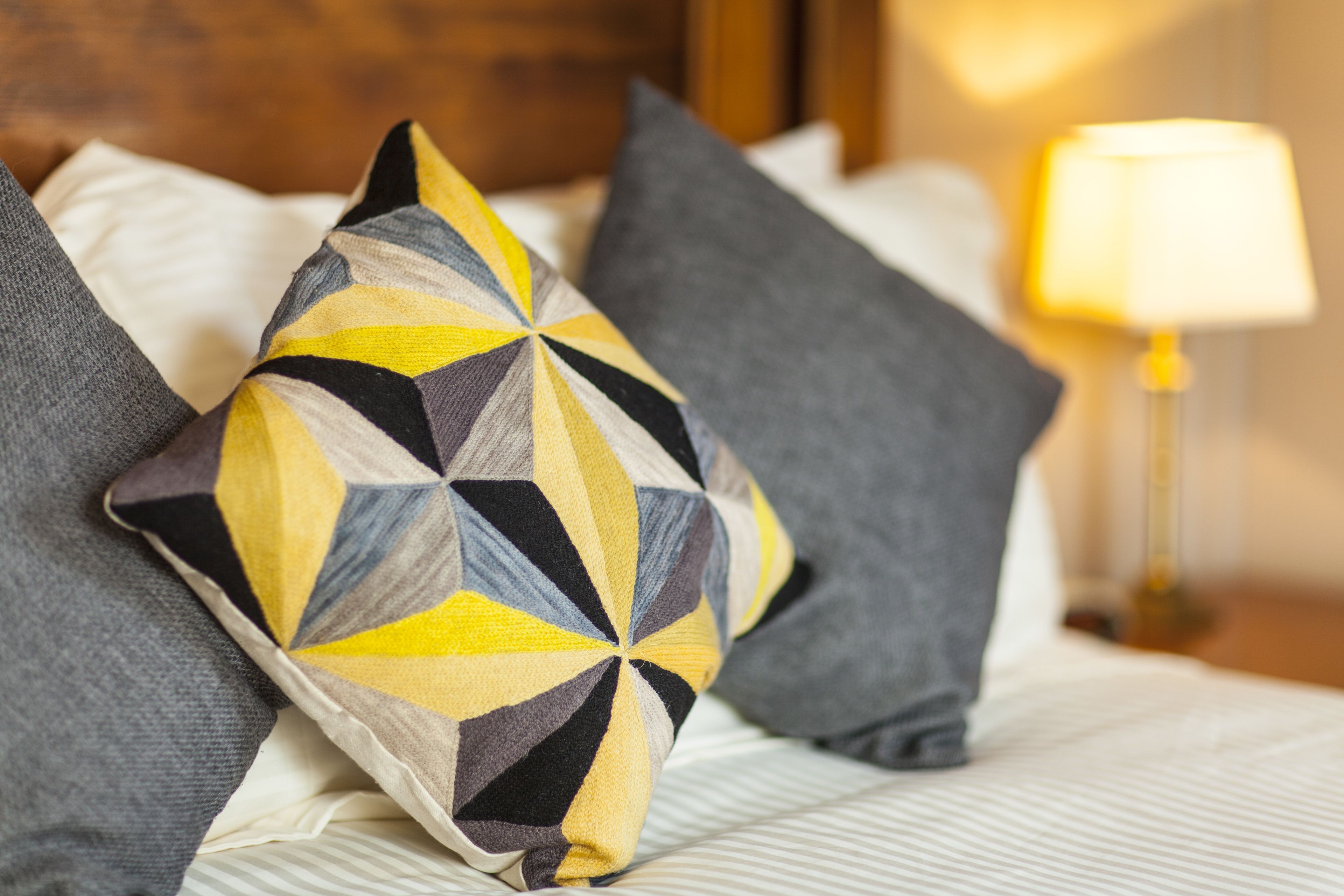Ein Bett mit einem gemusterten Kopfkissen, einer Lampe und einem Holzkopfbrett.