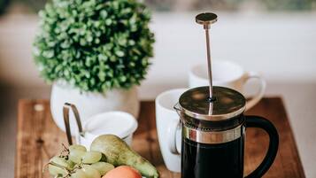 A coffee maker, a bowl of fruit, and a small potted plant on a wooden table.