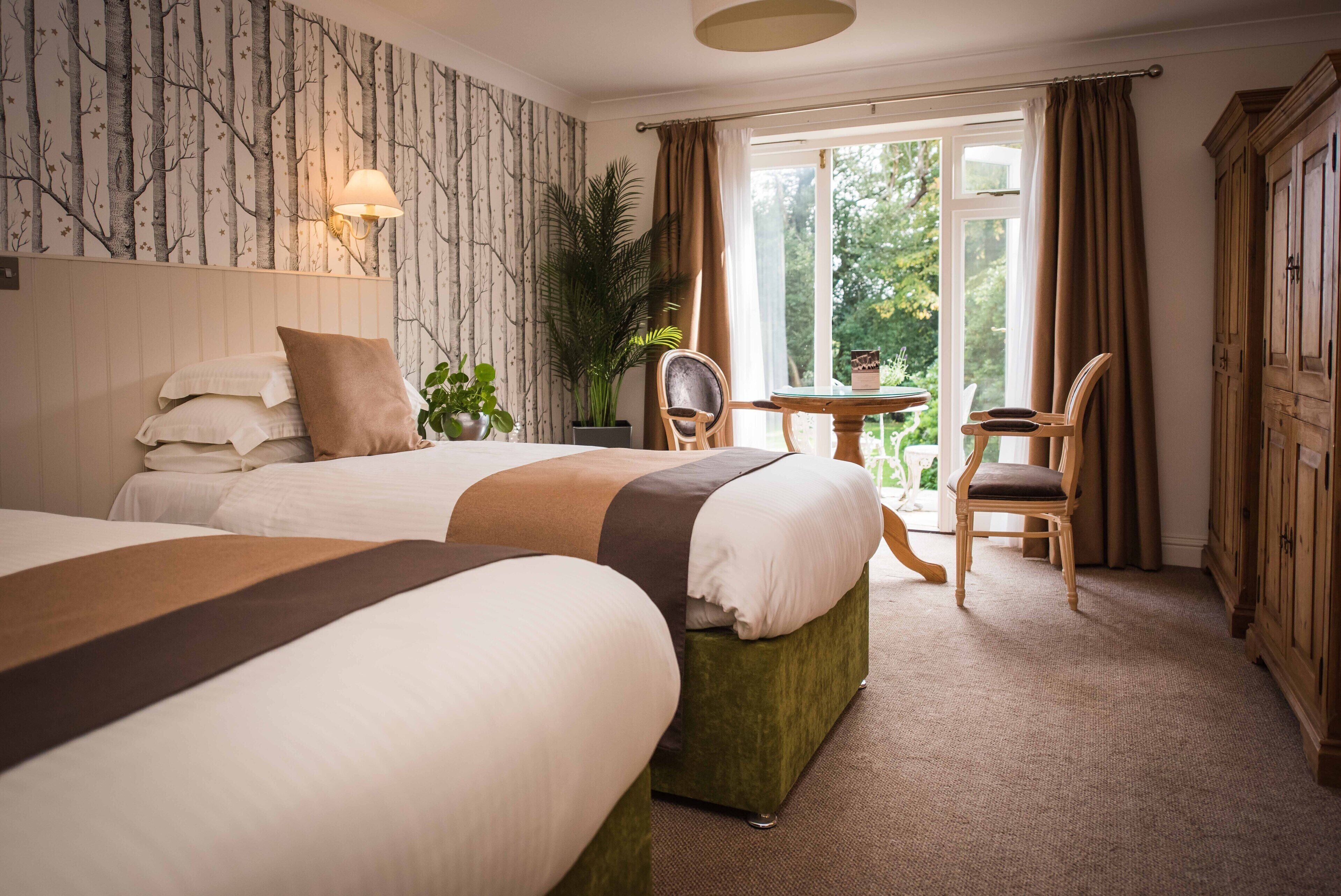 Ein Hotelzimmer mit zwei Betten, einem Esstisch, Stühlen, einer Topfpflanze und Blick ins Freie.