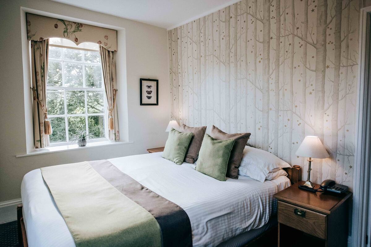 A neatly made bed with a striped bedspread, a bedside lamp, and a nightstand with a phone and a lamp.