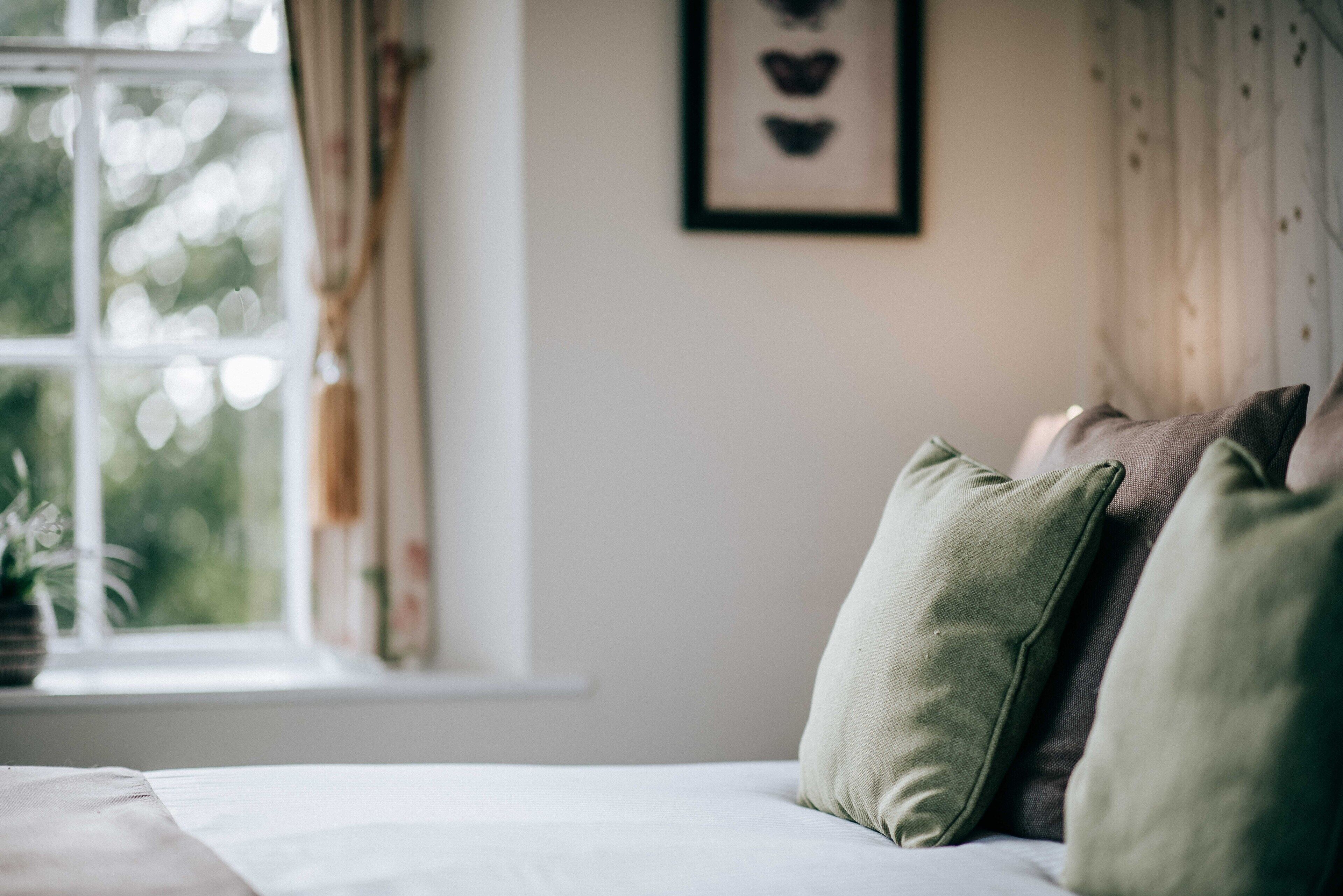 Un dormitorio con cama, almohadas, una ventana y un cuadro en la pared.