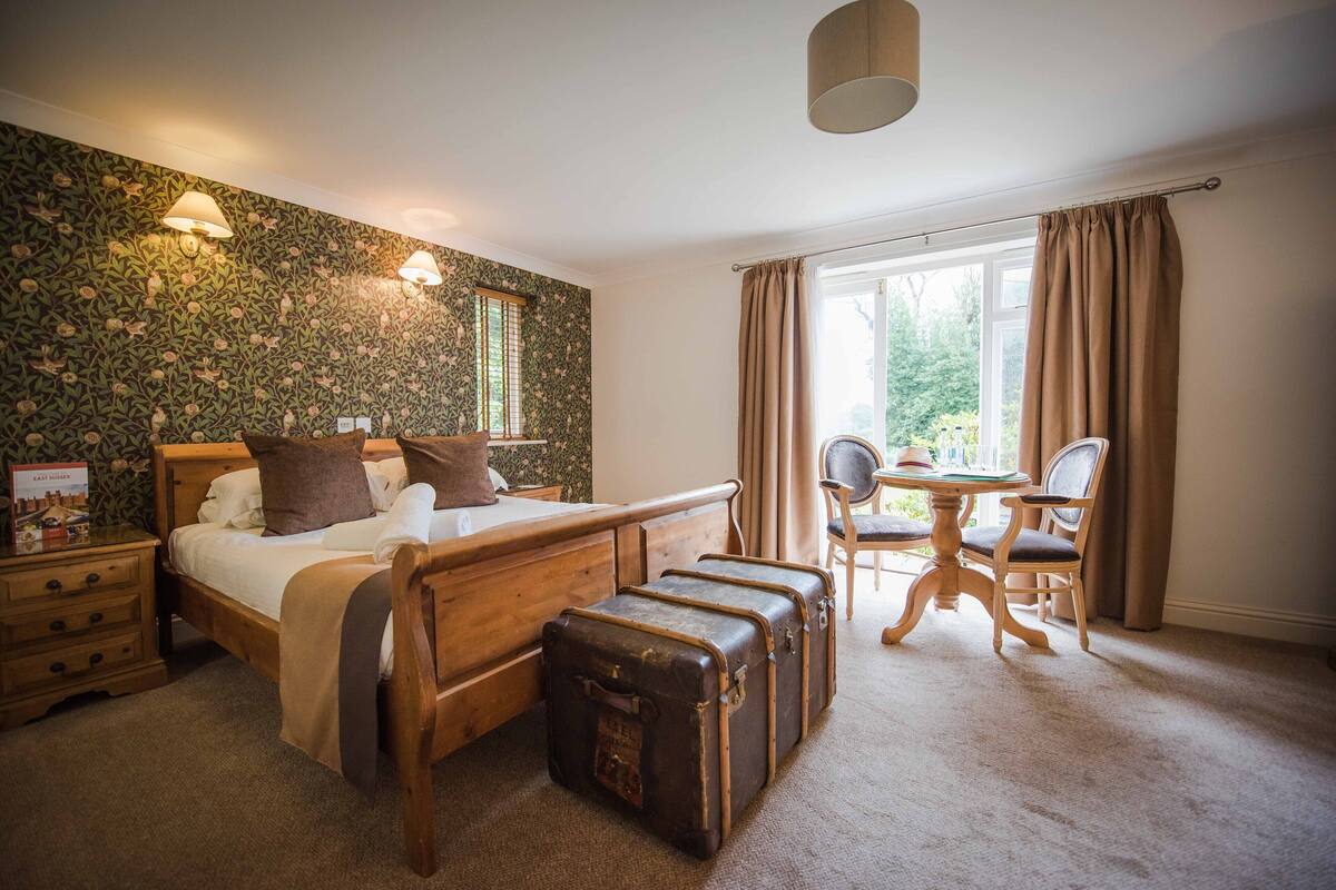 A bedroom with a bed, a wooden dresser, a desk with a chair, and two vintage suitcases.