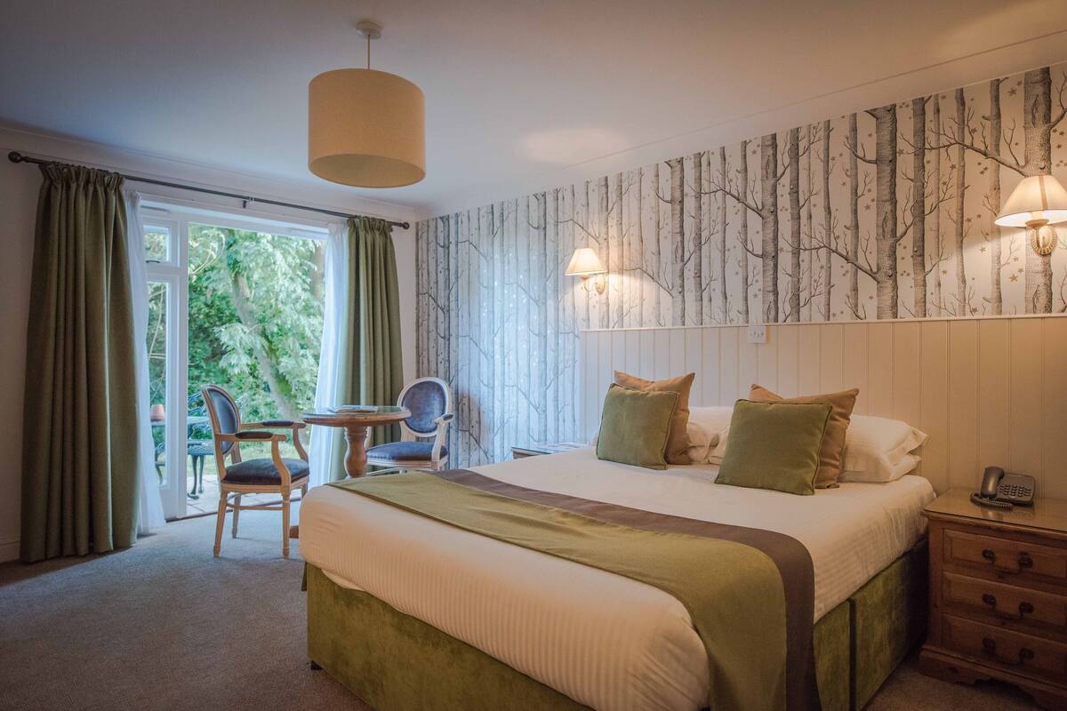 A bedroom with a large bed, a chair, a table, and a view of the outdoors.