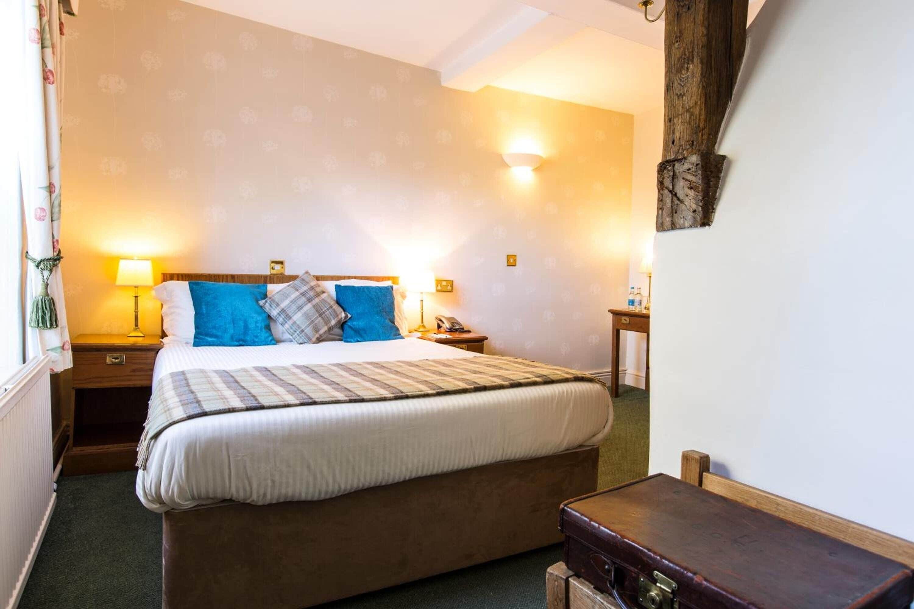 A bedroom with a bed, bedside lamps, a wooden nightstand, a dresser, and a wall-mounted light fixture.
