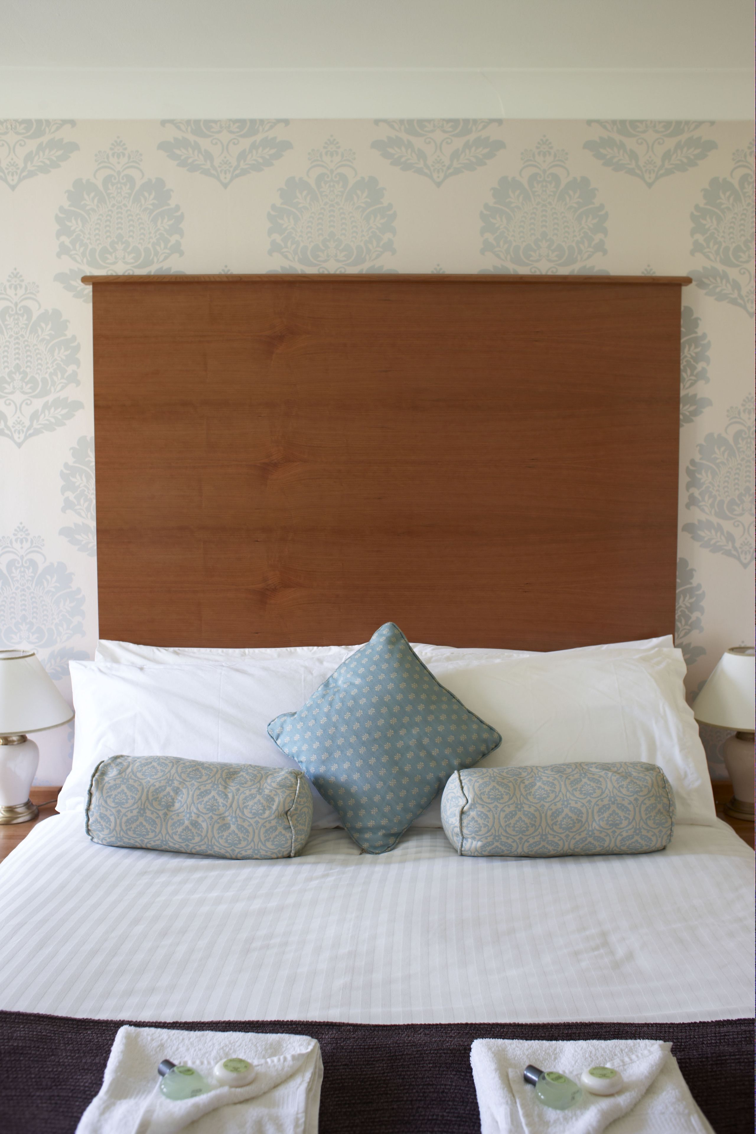 A neatly made bed with a wooden headboard, two patterned pillows, and a white comforter.