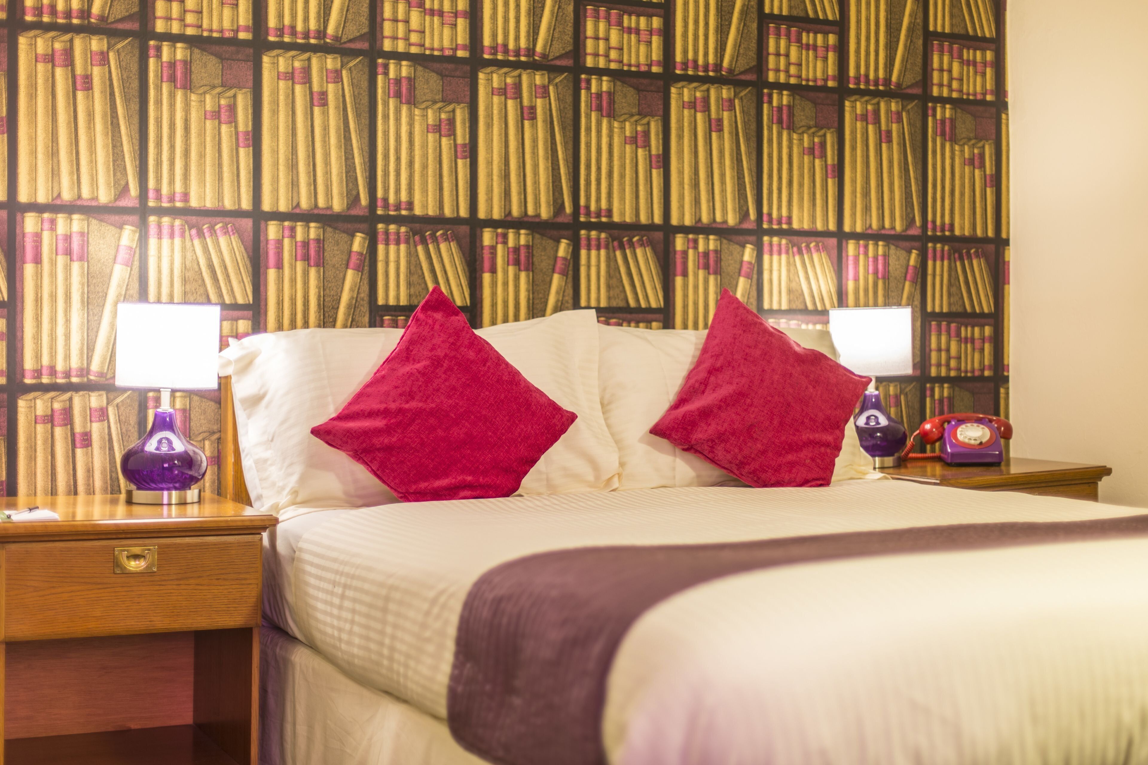 A hotel room with a large bed, two nightstands, a bookshelf, and a classic telephone.