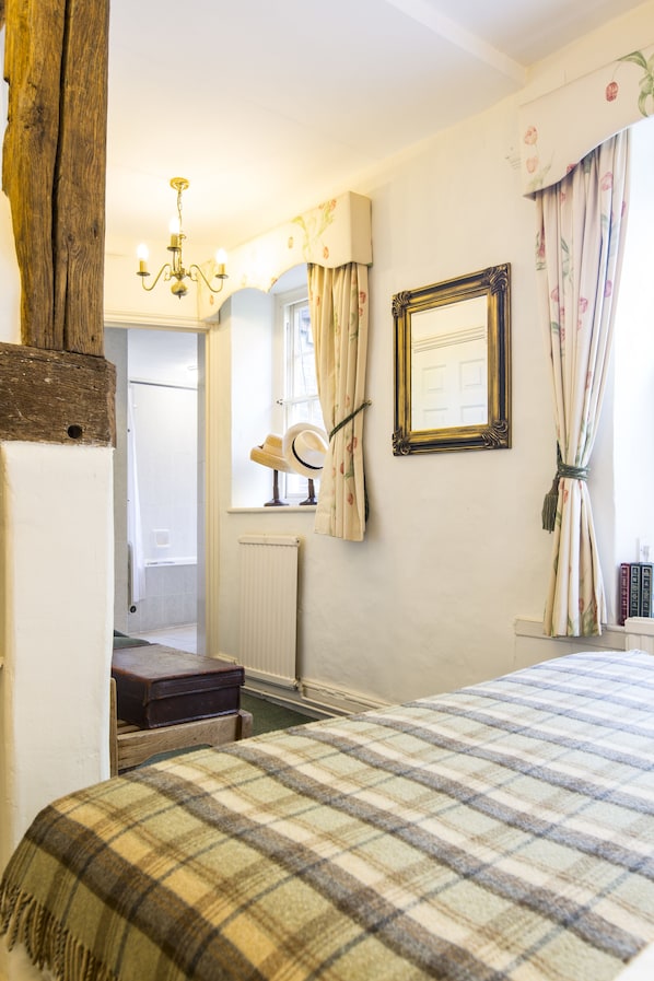 Un dormitorio con colcha escocesa, cabecero de madera, candelabro, espejo y radiador.