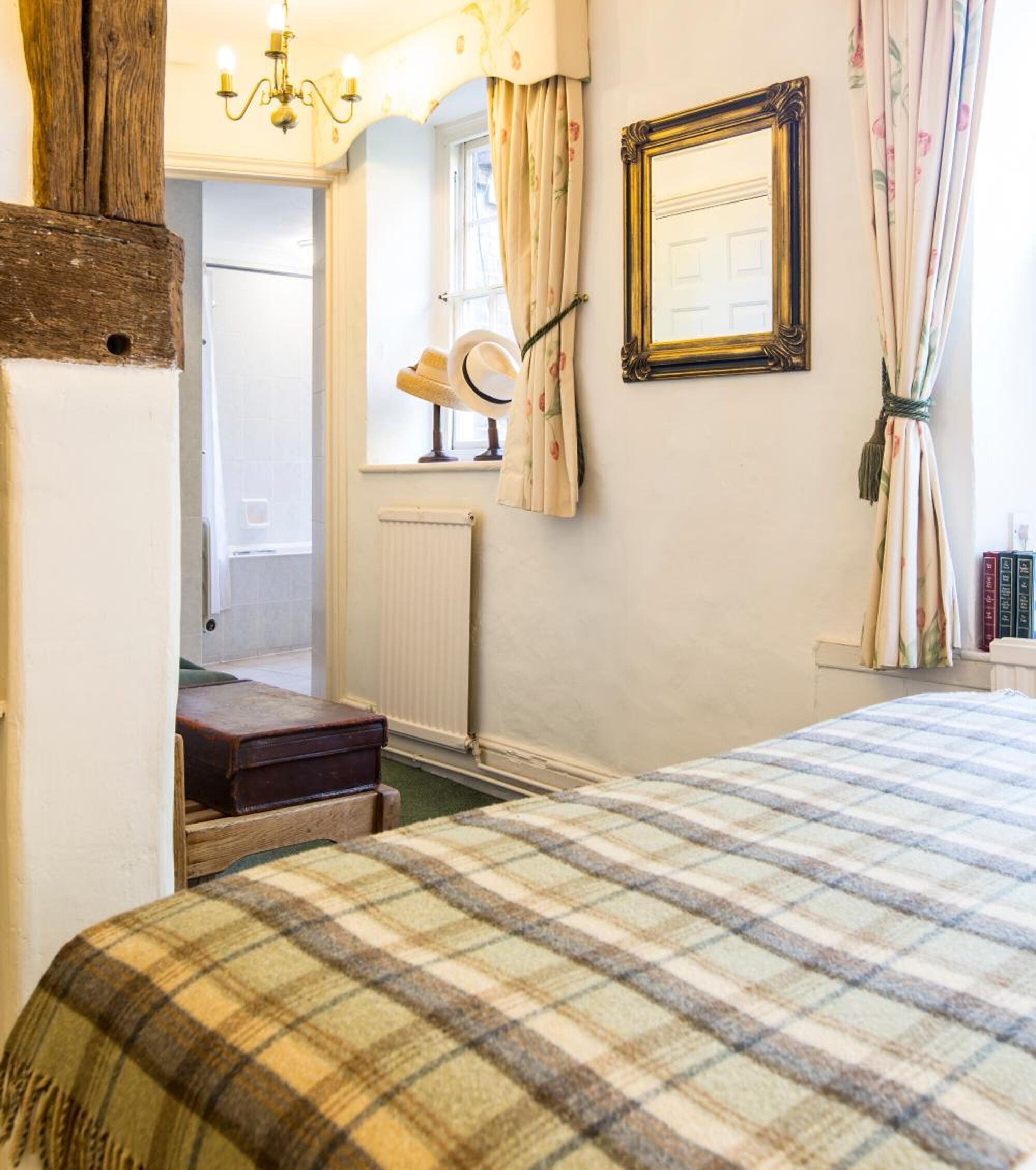 A bedroom with a plaid bedspread, a wooden headboard, a mirror, and a radiator.