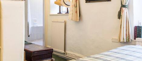 A bedroom with a plaid bedspread, a wooden headboard, a mirror, and a radiator.