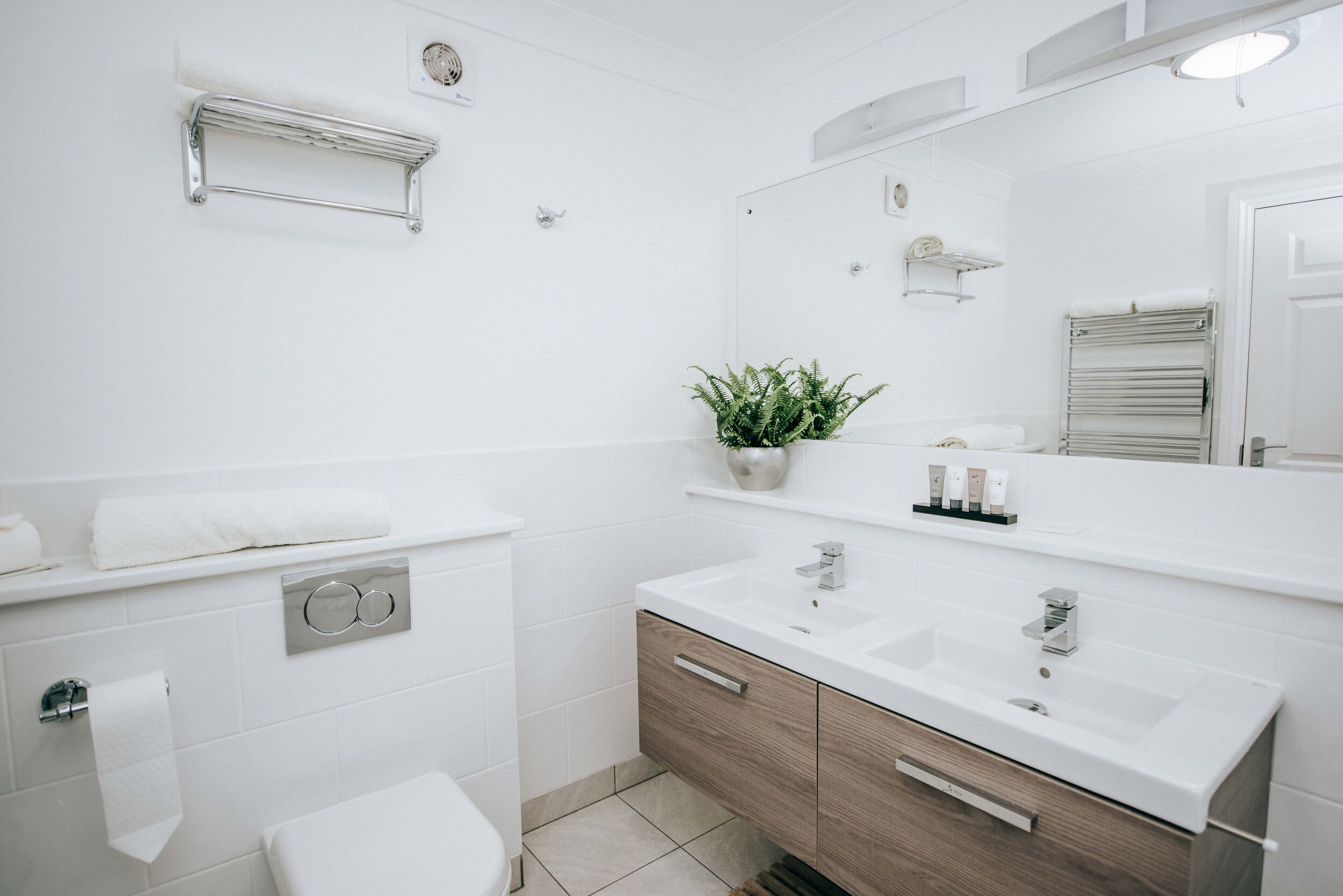 A modern bathroom with white tiles, a wooden vanity, a large mirror, and a plant.
