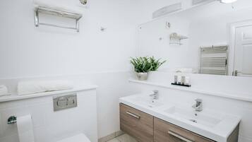 A modern bathroom with white tiles, a wooden vanity, a large mirror, and a plant.