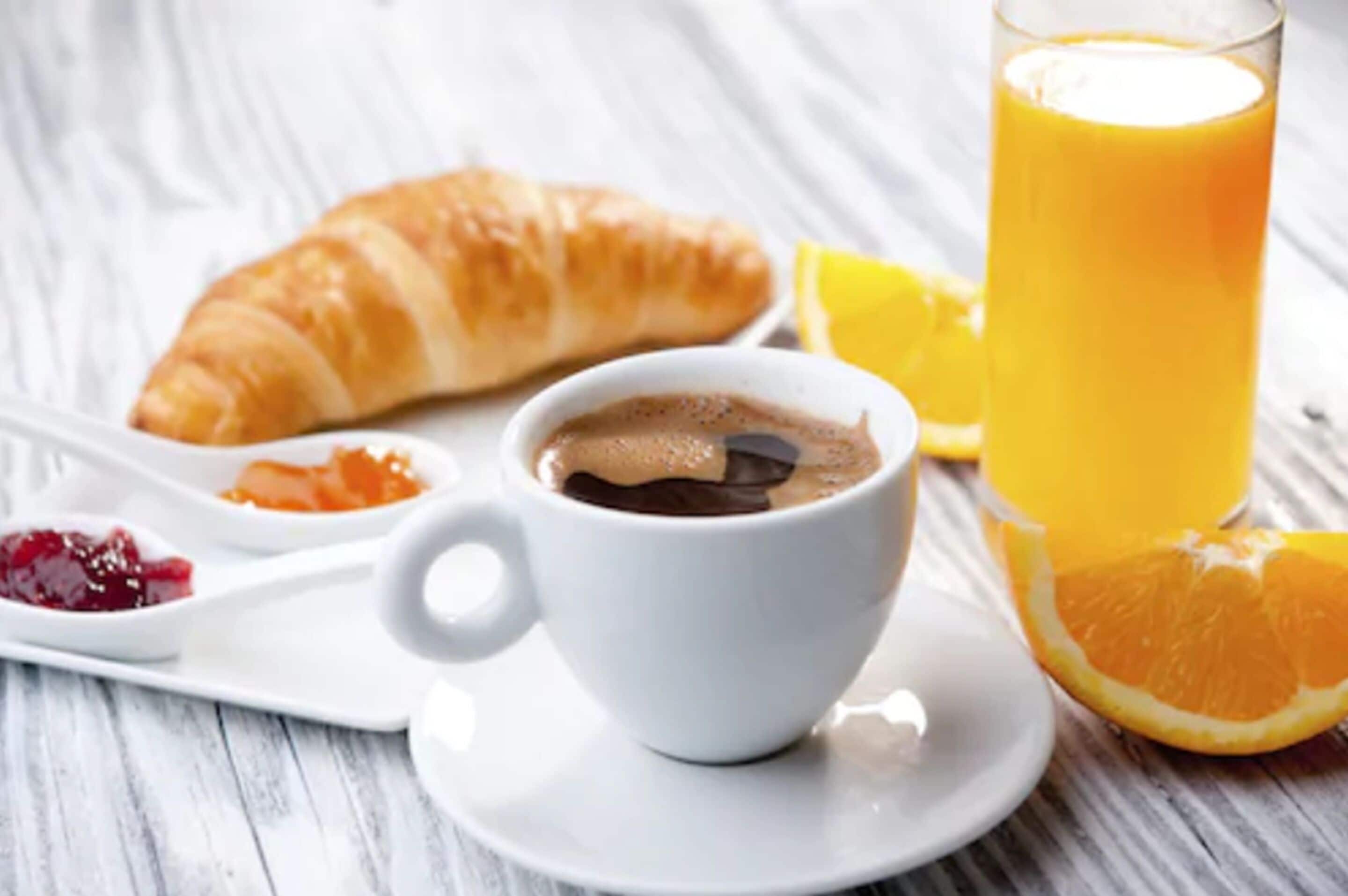 Ein Croissant, eine Tasse Kaffee mit Schokolade und ein Glas Orangensaft auf einem weißen Teller.