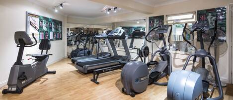 A gym with various exercise machines, including treadmills and elliptical trainers, on a wooden floor.
