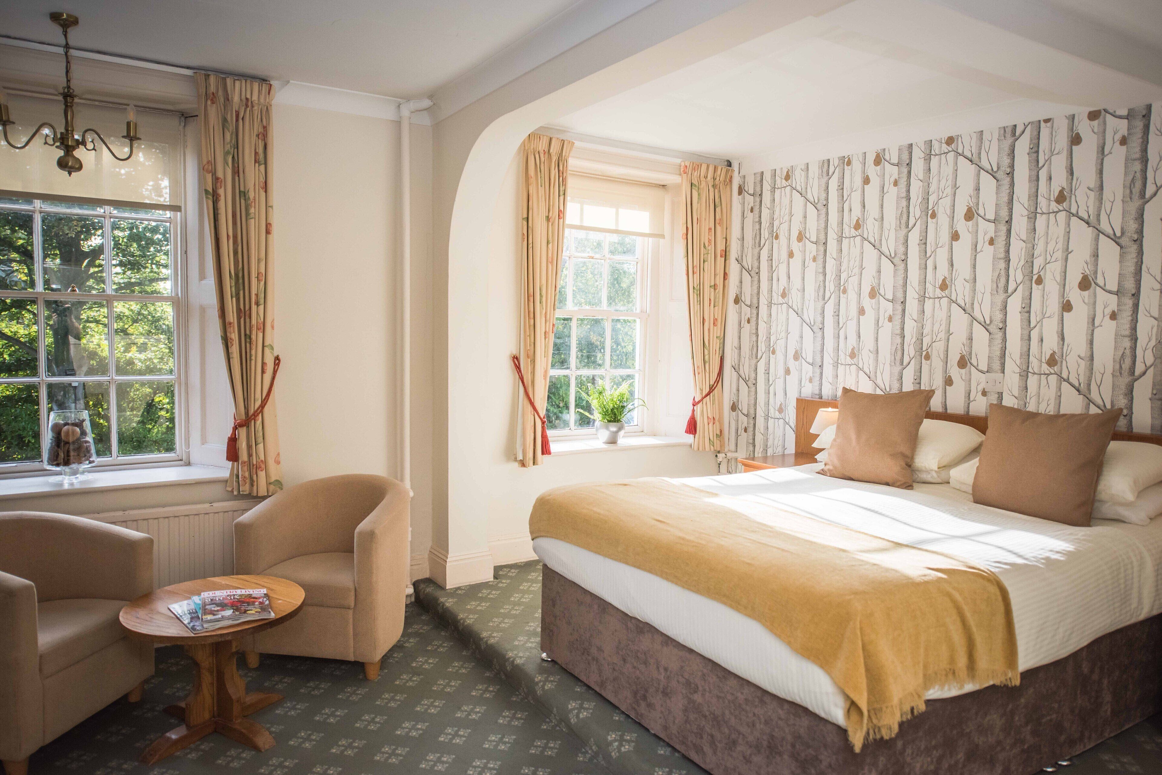 A bedroom with a large bed, two armchairs, a small table, and a window with curtains.