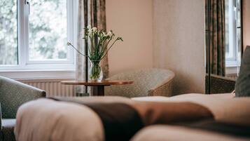 Una habitación acogedora con un sofá, una mesita redonda con un florero y una ventana con cortinas.