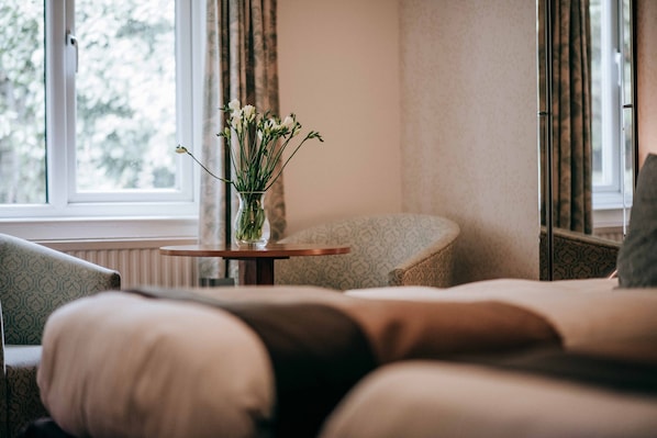 A cozy room with a sofa, a small round table with a vase of flowers, and a window with curtains. - Flackley Ash Country House Hotel (Rye)