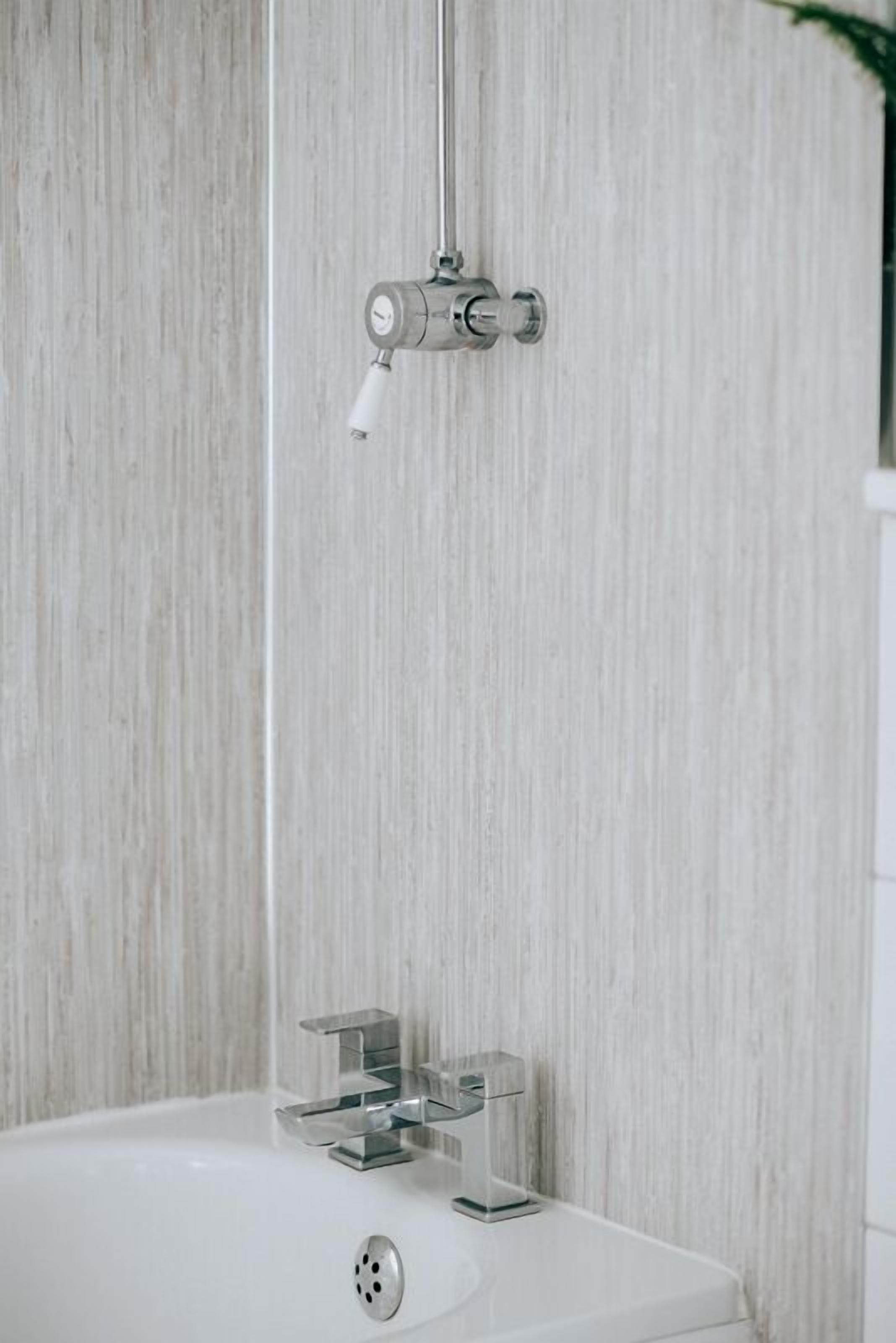 Une salle de bain avec une baignoire blanche, un robinet moderne et une pomme de douche fixée sur un mur en bois.