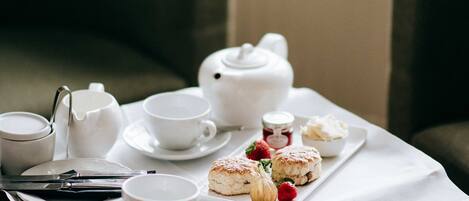 Una mesa servida para tomar té, con tazas, tetera y bollos.